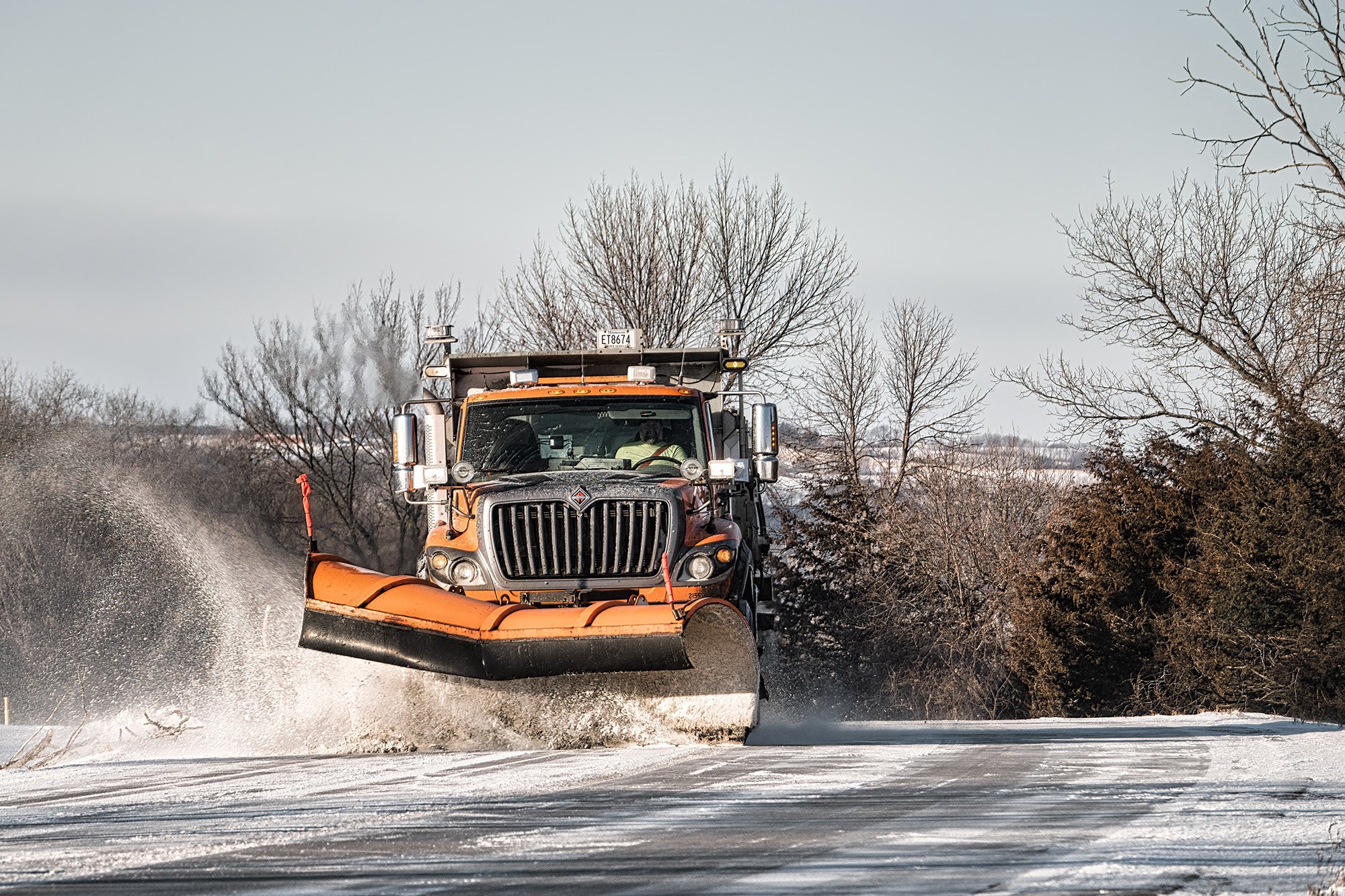 A snowplow driving down a highway plowing snow.